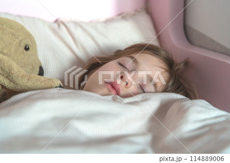 cute little girl sleeps in bed with soft toy 114889006