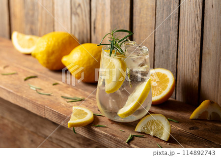 Summer refreshing drink with ice, rosemary and lemon slices on a old wooden table. 114892743