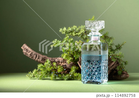 Blue gin in decanter on a background of old snags and juniper branches with berries. 114892758