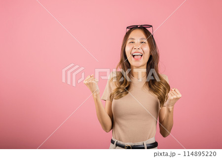 Happy Asian portrait beautiful cute young woman wear glasses makes raised hand up celebrating her winning success gesture, studio shot isolated pink background, Female excited say yes with copy space 114895220