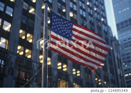 US flag flying in city street amidst towering buildings 114895349