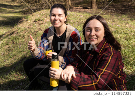 two young women on a picnic, sitting with a yellow thermos 114897325