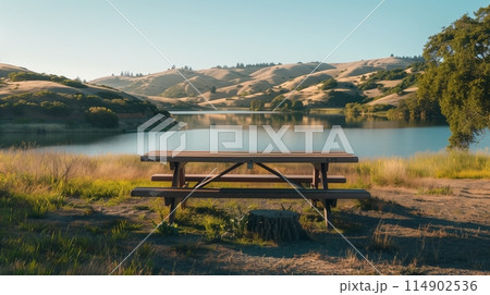 Serene Lakeside Picnic Spot: Wooden table/benches, scenic hills - perfect road trip pause. 114902536