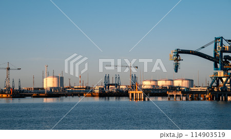 A large blue crane is lifting a large container from a ship A large blue crane is lifting a large container from a ship 114903519