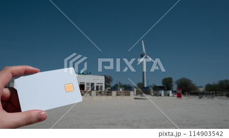 A person holding a credit card in front of a wind turbine 114903542