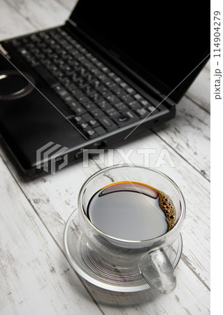 ガラス製のコーヒーカップとノートパソコンを縦構図で ガラス製のコーヒーカップとノートパソコンを縦構図で 114904279