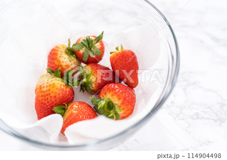 Freshly washed and dried strawberries are carefully arranged in a glass bowl lined with paper towel, ready for snacking or further use. 114904498