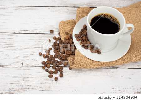 白い木目テーブルの上に置かれた麻袋、コーヒーカップとコーヒー豆 白い木目テーブルの上に置かれた麻袋、コーヒーカップとコーヒー豆 114904904