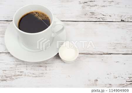 白い木目テーブルの上に置かれたコーヒーカップとコーヒーフレッシュ 白い木目テーブルの上に置かれたコーヒーカップとコーヒーフレッシュ 114904909