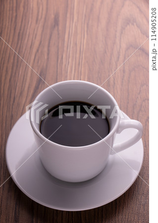 木目テーブルの上に置かれた白いカップのブラックコーヒーを縦位置で 114905208