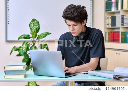 Portrait of college student guy sitting at desk with laptop inside an educational library Portrait of college student guy sitting at desk with laptop inside an educational library 114905505