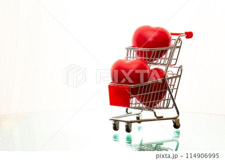 Miniature shopping cart filled with red heart shapes, symbolizing love, shopping, and Valentine's Day themes 114906995