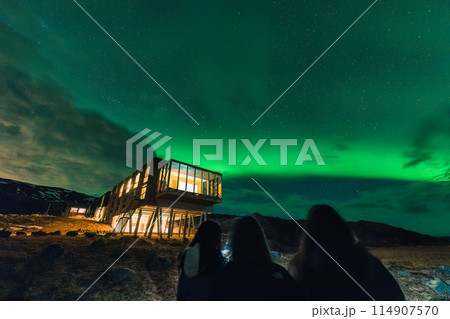 Aurora borealis glowing over luxury hotel and group of tourist friends looking at Iceland 114907570