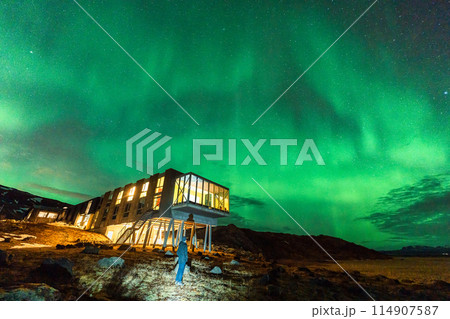 Aurora borealis, Northern lights glowing over luxury hotel and male tourist enjoying on mount Hengill in winter at Iceland 114907587