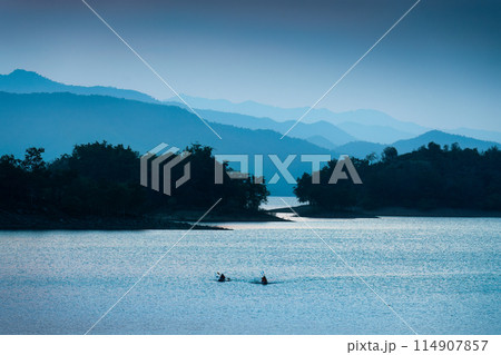 Blue scene of the Kaeng Krachan reservoir with fishing boat and tourist rowing canoe Blue scene of the Kaeng Krachan reservoir with fishing boat and tourist rowing canoe 114907857
