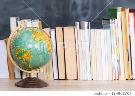 Globe on a chalkboard background. Books arranged vertically in one row on the desk. 114908707