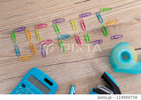 The inscription - office, made of colorful paper clips lying on a wooden desk top. Calculator and other office accessories. 114908756