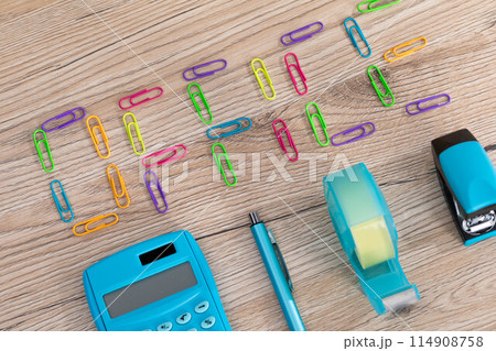 The inscription - office, made of colorful paper clips lying on a wooden desk top. Calculator and other office accessories. 114908758