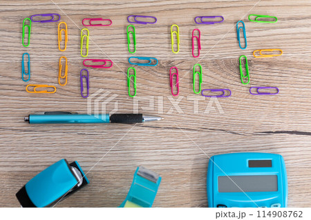 The inscription - office, made of colorful paper clips lying on a wooden desk top. Calculator and other office accessories. The inscription - office, made of colorful paper clips lying on a wooden desk top. Calculator and other office accessories. 114908762