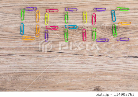 The inscription - office, made of colorful paper clips lying on a wooden desk top. 114908763