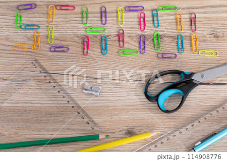 Inscription - school made of colorful office paper clips. Basic school supplies lie on the top of the school bench. 114908776