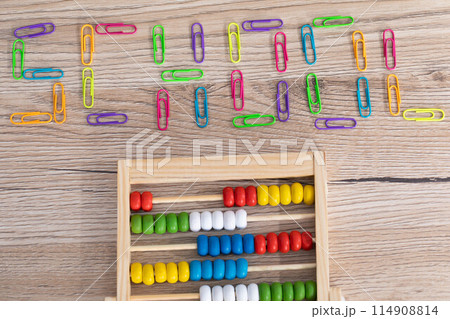 Colorful paper clips arranged in an inscription - school. Wooden top of the school desk. Counters for counting. Colorful paper clips arranged in an inscription - school. Wooden top of the school desk. Counters for counting. 114908814