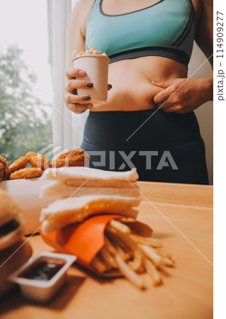 To eat or not. Cheerless plump woman looking at the burger while thinking to eat it or not 114909277