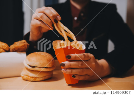 Asian woman holding french fries and eating happily in restaurant Asian woman holding french fries and eating happily in restaurant 114909307