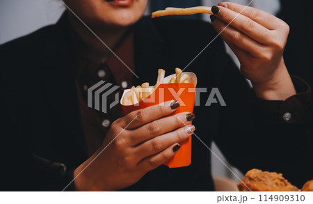 Asian woman holding french fries and eating happily in restaurant 114909310