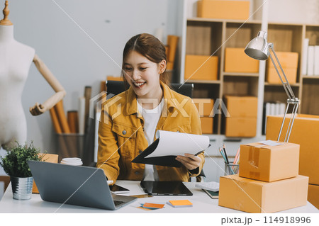 Asian SME business women use laptop computer checking customer order online shipping boxes at home. Starting Small business entrepreneur SME freelance. Online business, Work at home concept. Asian SME business women use laptop computer checking customer order online shipping boxes at home. Starting Small business entrepreneur SME freelance. Online business, Work at home concept. 114918996