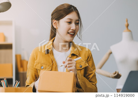 Asian SME business women use laptop computer checking customer order online shipping boxes at home. Starting Small business entrepreneur SME freelance. Online business, Work at home concept. Asian SME business women use laptop computer checking customer order online shipping boxes at home. Starting Small business entrepreneur SME freelance. Online business, Work at home concept. 114919000