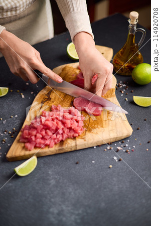 Woman cut tuna steak into slices on a wooden cutting board at domestic kitchen 114920708