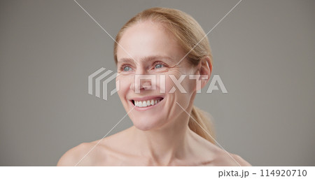 Real people - concept of age, beauty, health and dry skin care - beautiful mature Caucasian middle-aged woman in her 50s looks with a calm confident look at the camera, smiles a bright toothy smile 114920710