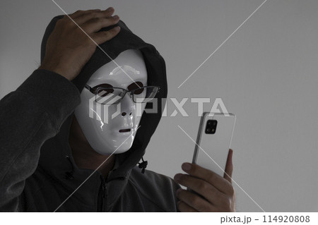 白い仮面と眼鏡をつけスマートフォンを持つ男性。頭を抱える 白い仮面と眼鏡をつけスマートフォンを持つ男性。頭を抱える 114920808