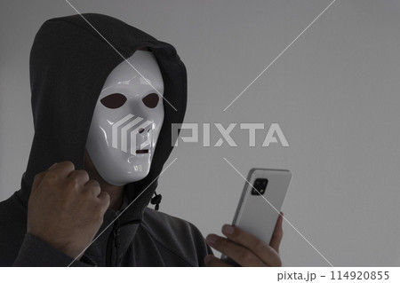 白い仮面をつけスマートフォンを持つ男性。握りこぶし 白い仮面をつけスマートフォンを持つ男性。握りこぶし 114920855