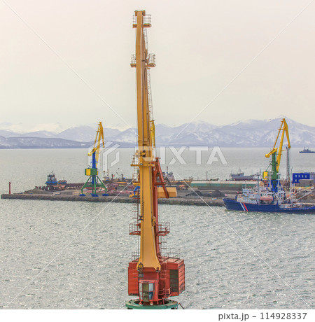 Port cranes and ships on commercial seaport Petropavlovsk-Kamchatsky City on shore of Avacha Bay in Pacific Ocean. Port cranes and ships on commercial seaport Petropavlovsk-Kamchatsky City on shore of Avacha Bay in Pacific Ocean. 114928337
