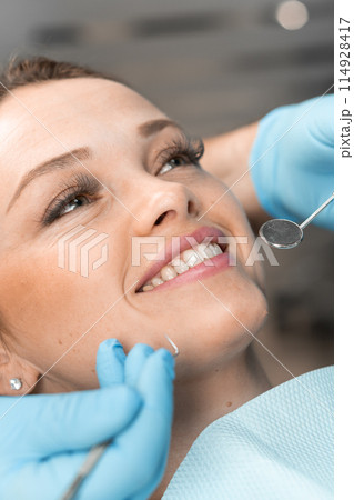 A patient in dental chair rejoices in her new smile. A dentist, looking closely at result, provides high-quality dental care that not only solves problems, but also gives confidence to the patient. 114928417