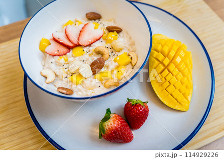 A bowl of oats with strawberries and mango arranged on a plate 114929226