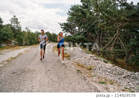 A couple dressed in sportswear runs along a scenic road during an early morning workout, enjoying the fresh air and maintaining a healthy lifestyle 114929579