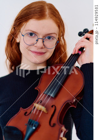 Stunning Redhead Musician Poses with Violin in Captivating Portrait 114929581