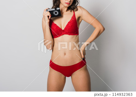 Beautiful female with pretty smile in red lingerie holding photo camera, isolated on white Beautiful female with pretty smile in red lingerie holding photo camera, isolated on white 114932363