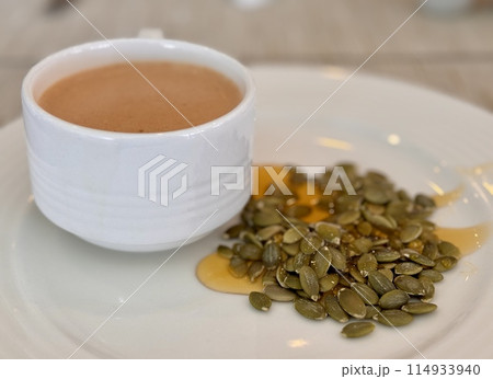 A cup of coffee sits beside a sound of pumpkin seeds poured with liquid lime honey, showcasing a contract between the liquid beverage and the solid ingredient at the table. Close-up 114933940