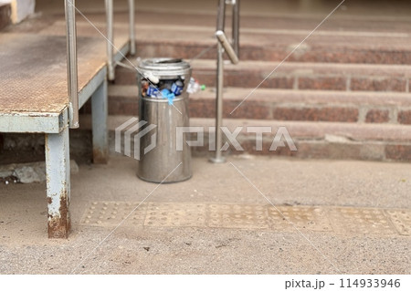 Overflowing trash can and scattered garbage on a sidewalk next to stairs next to supermarket 114933946