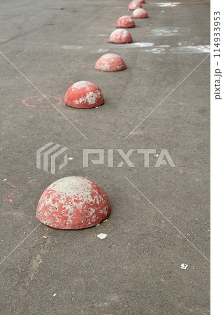 Red restrictive hemispheres on the asphalt road in the parking area of the car and the pedestrian area of walking people at the street. Area for foot people 114933953