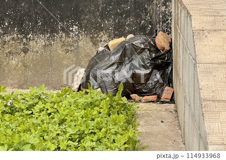 Under a residential apartment building next to the stairs there is a black garbage bag covered with building bricks in the corner of the house Under a residential apartment building next to the stairs there is a black garbage bag covered with building bricks in the corner of the house 114933968