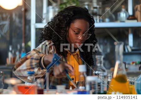 Black girl doing a science experiment in school, at a desk with test tubes and beakers, wearing glasses, with a chalkboard background showing a globe and educational posters 114935141