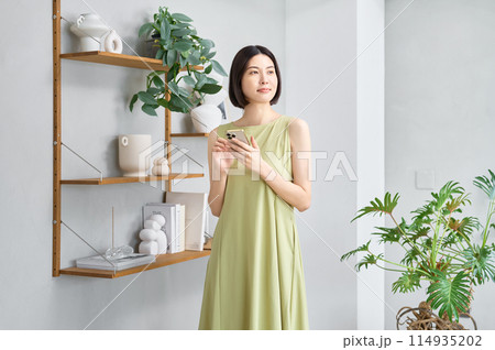 部屋でスマホを操作する夏服の若い女性 部屋でスマホを操作する夏服の若い女性 114935202