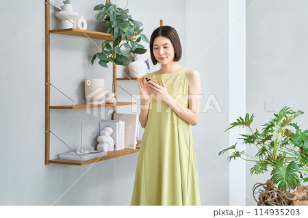 部屋でスマホを操作する夏服の若い女性 部屋でスマホを操作する夏服の若い女性 114935203