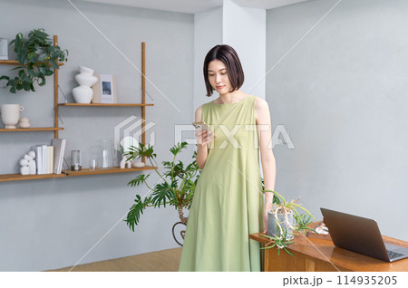 部屋でスマホを操作する夏服の若い女性 114935205