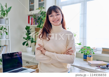 Portrait of smiling female student, 19,20 years old, looking at camera, in home interior Portrait of smiling female student, 19,20 years old, looking at camera, in home interior 114936650